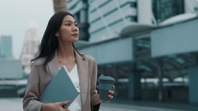 Portrait of young Asian woman with laptop and coffee cup walking along street. Thoughtful Thai business lady holds computer and drink near office center. Successful commercial career - Powered by Shutterstock - Get 15% off with code: PIKWIZARD15