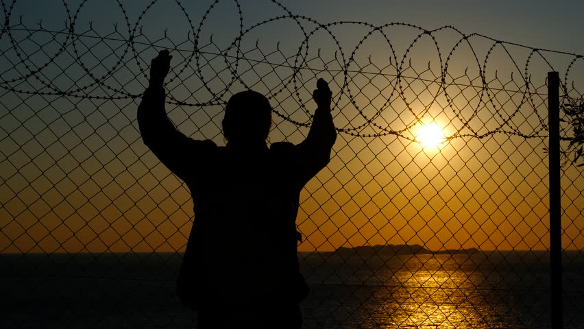Refugee silhouette standing behind barbed wire fence. Raising arms triumphantly against golden sunset sky. Embodying hope. Liberation. And transformative journey toward freedom and new opportunities