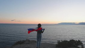A brunette woman with a Russian flag on her shoulders stands on a rocky seashore at sunset. Gives independence, patriotic holiday concept. - Powered by Shutterstock - Get 15% off with code: PIKWIZARD15