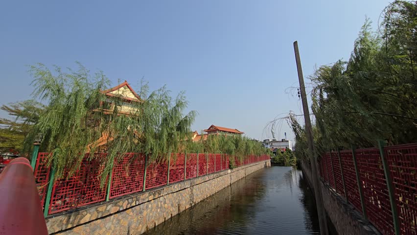 A quiet canal beside Wat Boromracha Kanchanaphisek, lined with red walls and lush greenery