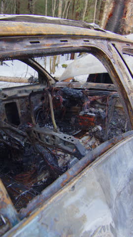 Crashed and burned out car wreck on snowy roadside, reckless driving. Vertical