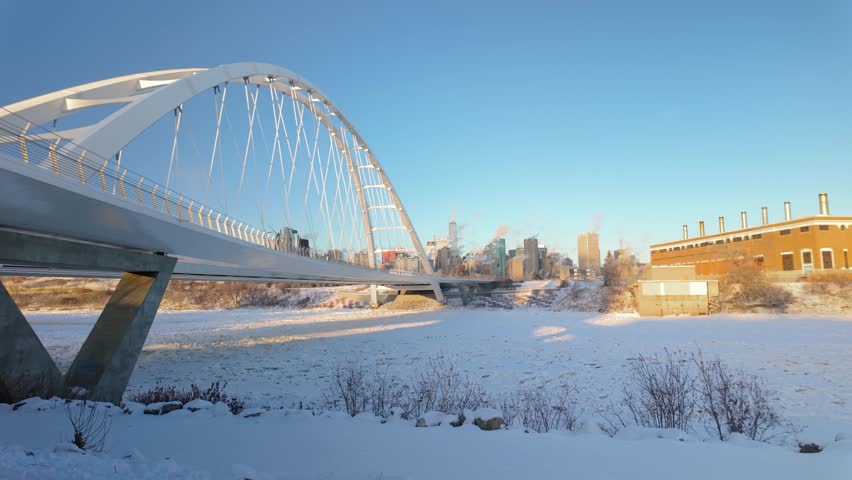 A freezing winter day in Downtown Edmonton, viewed from the Walterdale Bridge, showcasing Highrise buildings, a snowy river valley, and the cold beauty of the city