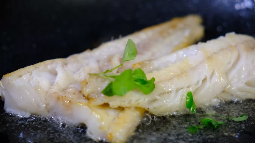Cooking Indoors pan grilled seasoned Cod fillets on Stovetop, iron cast pan, close up boiled oil, deep fried. White meat 