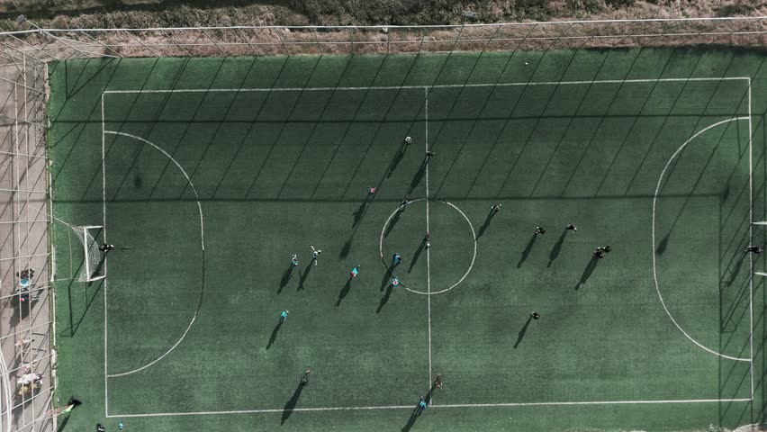 Fun and relaxed game on small 5x5 soccer field with players exchanging passes and goalkeeper catching the ball, tilt down drone shot.