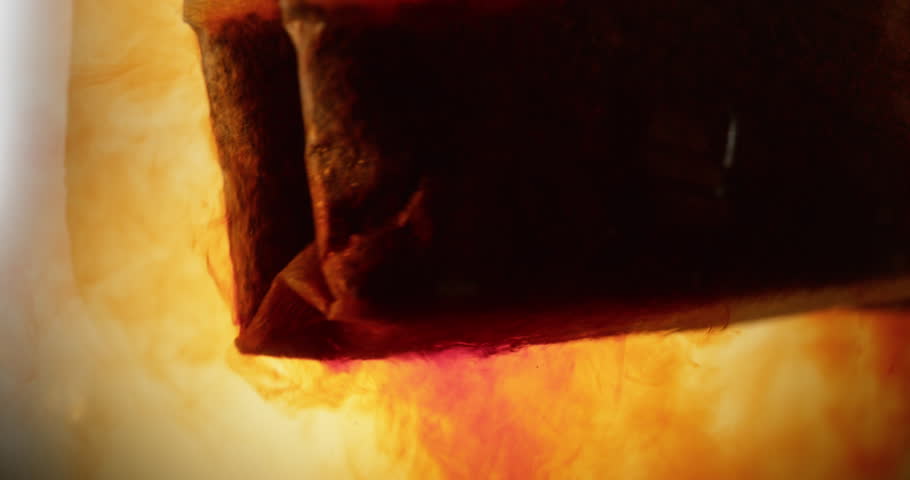 close up shot of a tea bag submerging inside a glass releasing its contents and coloring the liquid