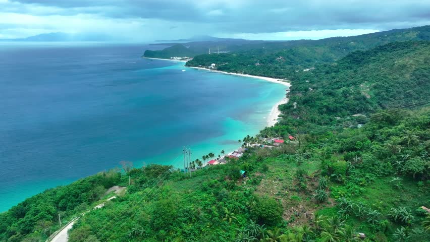 Colored houses and roofs in Puerto Galera with sandy beach on tropical island of Philippines. Aerial top down shot. Small town with turquoise ocean water.