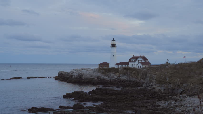 As the sun sets over Cape Elizabeth, Maine, a serene and breathtaking view of a lighthouse emerges, surrounded by a rugged coastline and tranquil waters, creating a truly picturesque scene