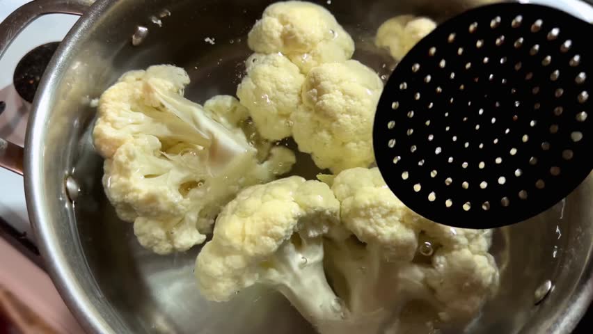 Cauliflower pieces in hot water during their blanching in the stainless steel pot on the stove top
