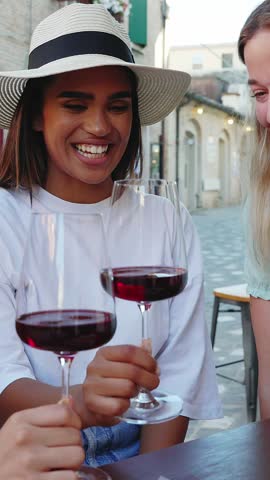 Vertical HD video of young happy diverse women friends enjoying time together toasting red wine and eating Italian aperitif in a restaurant. Friendship concept.