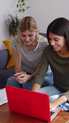 Vertical HD video of two happy young women planning vacation travel with laptop computer, using credit card booking tickets or hotel room on web. Summer holidays concept.