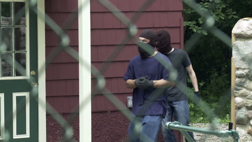 Two masked burglars make their way through an open gate and get into a house