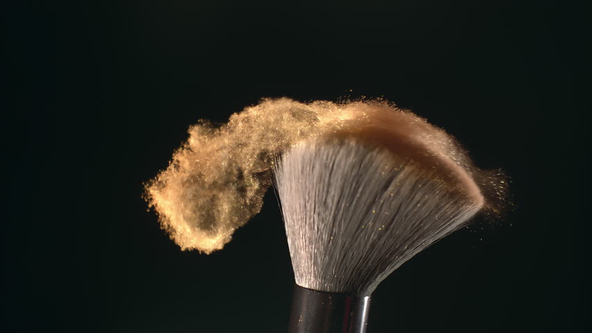 Super slow motion macro shot of makeup brush and golden shiny face powder shake at 1000 fps. Elegant luxury make up cosmetic abstract background. Beauty make-up glitter flying in high speed close up