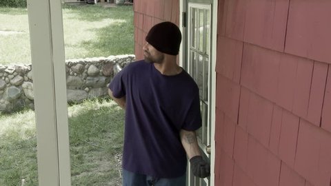 Burglar checks through garage window then goes around to door where he tries the handle and discovers the door is unlocked. Jib shot.