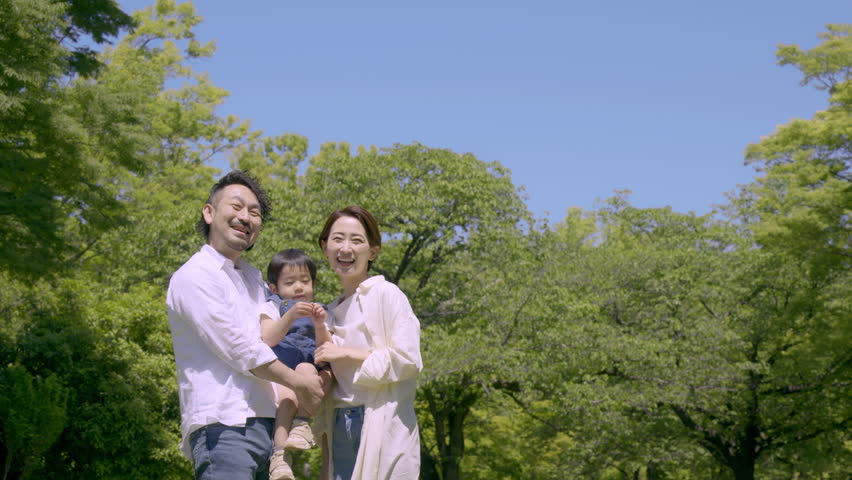 A Japanese family looking up at a fresh green park with blue sky. Image of moving and new life, relaxing, looking at the future and hope.