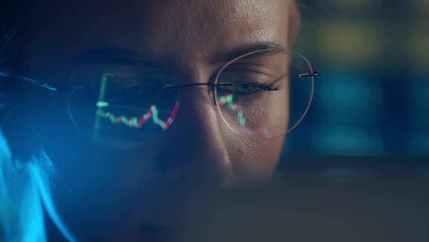 Trader wearing glasses is working on laptop computer. Screen with stock market charts and Bitcoin BTC or Ethereum ETH data analysis reflection. Broker trading online. Altcoins crypto currency trading