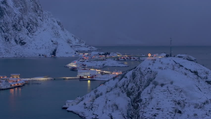 Aerial panoramic view of Hamnoy, an iconic fishing village in the Lofoten Islands, Norway, at dusk, illuminated cottages on the islands all connected by charming bridges over the fjord