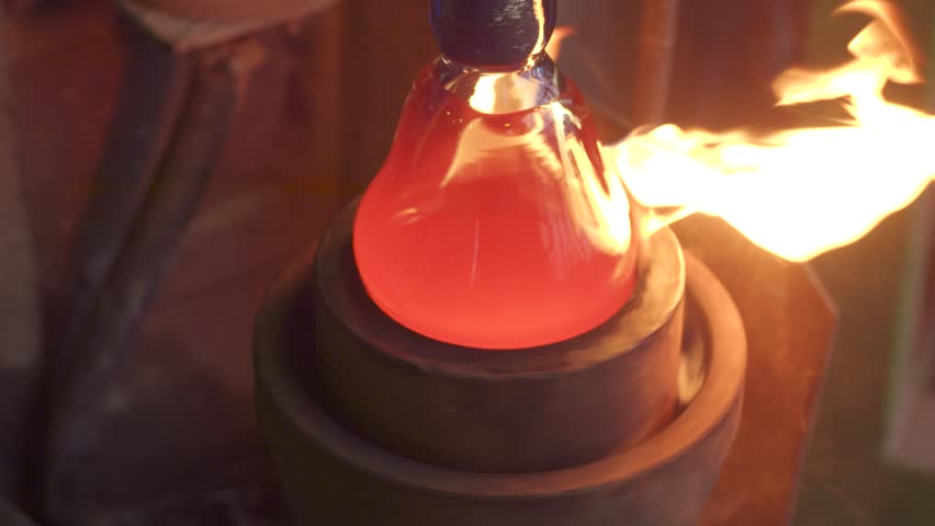 Manual glass production. Glassblower shaping molten glass with a torch in a workshop
