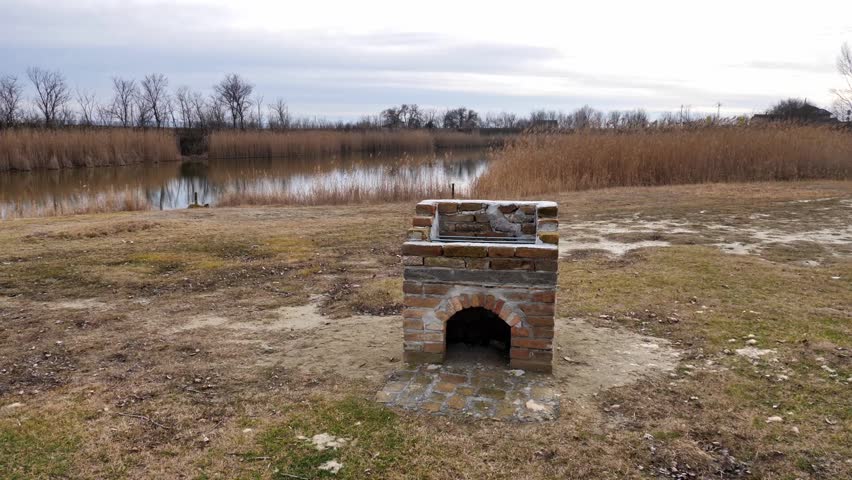 Old brick fireplace stands near tranquil water at a serene park location during a cool afternoon
