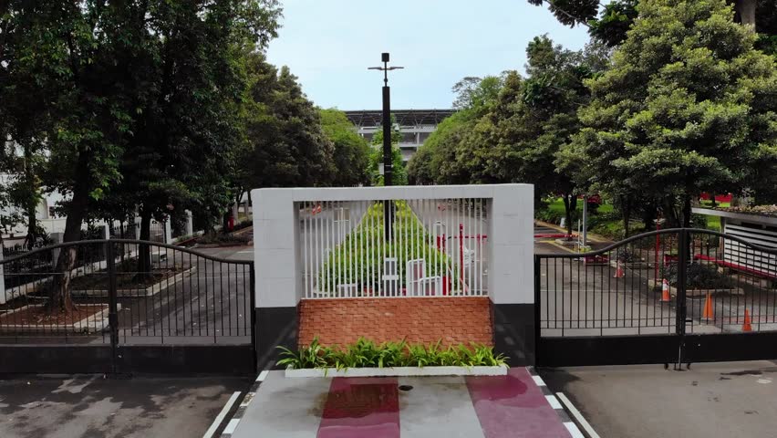 Aerial drone view of Gelora Bung Karno football stadium in Senayan, Jakarta. A lush sports center with lots of trees and views of skyscrapers.