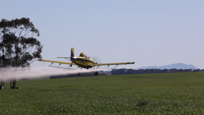 Crop duster airplane sprays field, soars into blue copy space sky