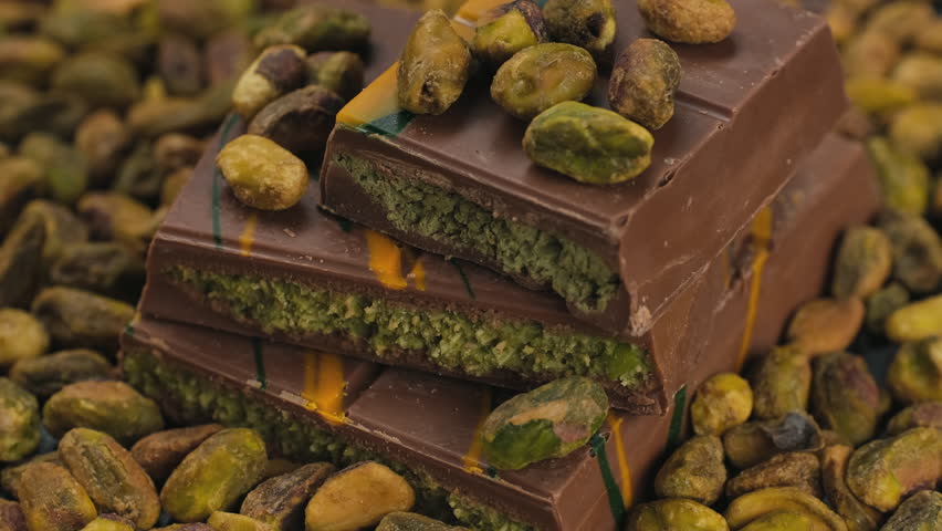 Chocolate bar with pistachio paste and whole pistachio nuts in plate, rotate