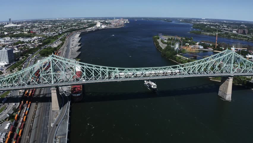 Aerial view of the Jacques Cartier Bridge in Montreal, spanning the St. Lawrence River. Its iconic design and connection between the island and the South Shore, with the city skyline in the backdrop.