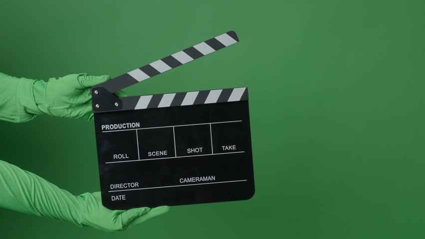 A classic black and white film clapperboard or movie slate being held in front of a green screen. Essential filmmaking tool is used to mark scenes and synchronize audio and video in film production.