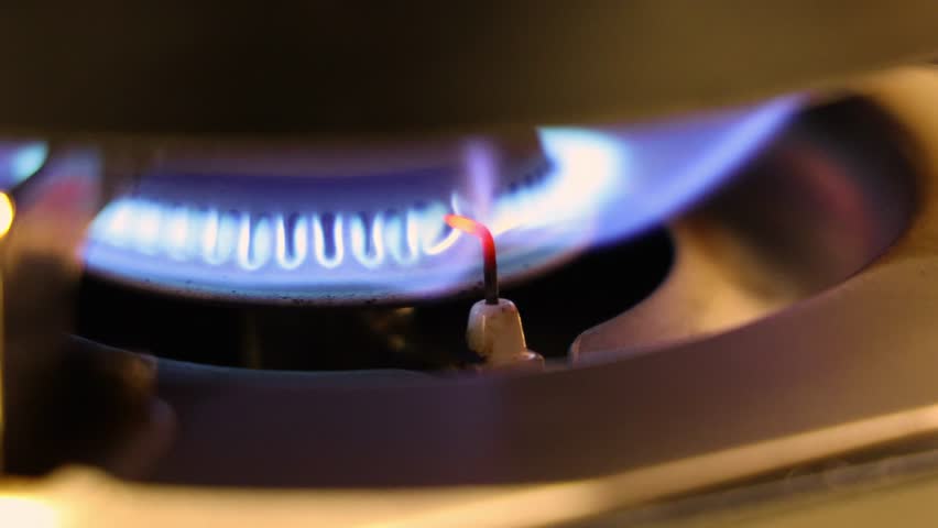 Gas stove flame. Close up of a gas stove burner igniting with a blue flame. Ignition electrode glows red hot as it sparks the fire. showing the process of controlled combustion in a kitchen gas stove.