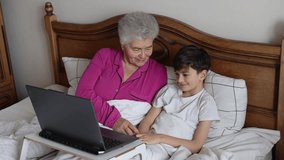 Grandmother and grandson sitting in bed, watching a video on a laptop. Cozy family moment, bonding across generations. Technology connects elderly and children in a warm, homey atmosphere - Powered by Shutterstock - Get 15% off with code: PIKWIZARD15