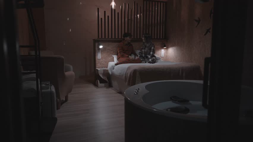 Romantic evening atmosphere in hotel room with young couple sitting on bed, talking and enjoying each other