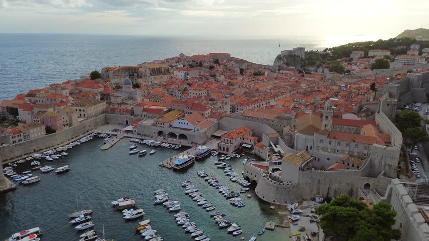 Dubrovnik harbor and cityscape with boats docked and people roaming walled streets, framed by scenic Adriatic views