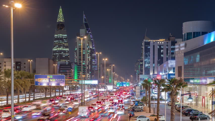 Cityscape aerial night timelapse of Riyadh, Saudi Arabia, featuring illuminated towers, skyscrapers, King Fahd Road and busy traffic. Palms and streetlights line the main highway through the city.