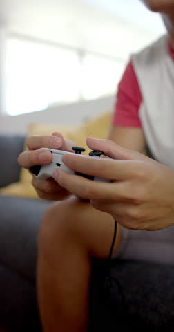 Vertical video: Celebrating victory, Asian teenage boy playing video game with headphones at home. Gaming, celebration, entertainment, slow motion