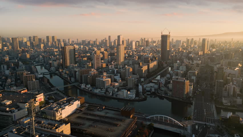osaka city central minami ward aerial view drone at sunrise,flying over kizu river,high-rise office buildings in the background,metropolis cityscape