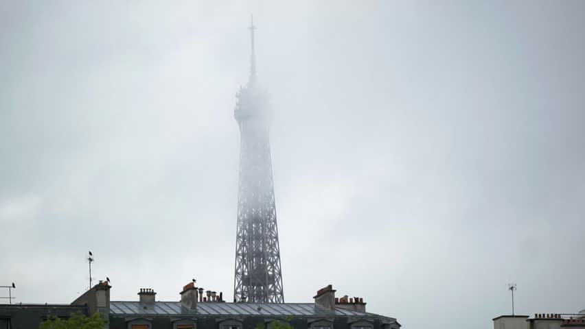 An early morning wide shot of the top of the eiffel tower in paris among clouds and fog