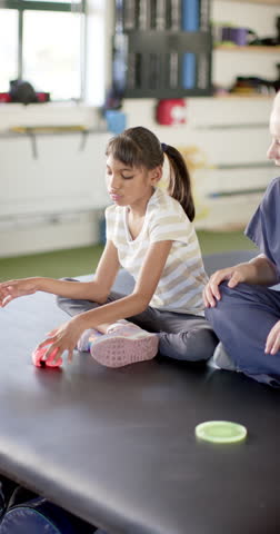 Vertical video: In disability rehab, girl playing with therapy toy while sitting with therapist. Physiotherapy, rehabilitation, healthcare, occupational therapy, child, treatment