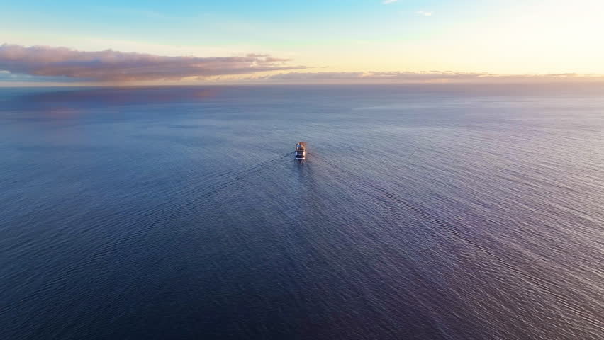 Sunset silhouette of a solitary ship navigating vast ocean waters during peaceful evening