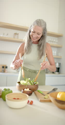 Vertical video: Preparing fresh salad, woman mixing ingredients in kitchen at home. Cooking, healthy, vegetables, lifestyle, nutrition, domestic, culinary, slow motion