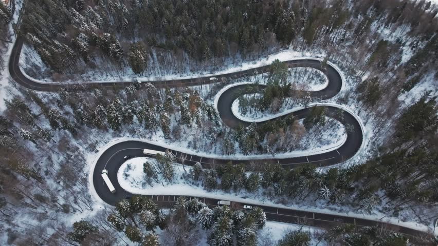 Winding road through snow-covered forest, aerial view of curves and turns