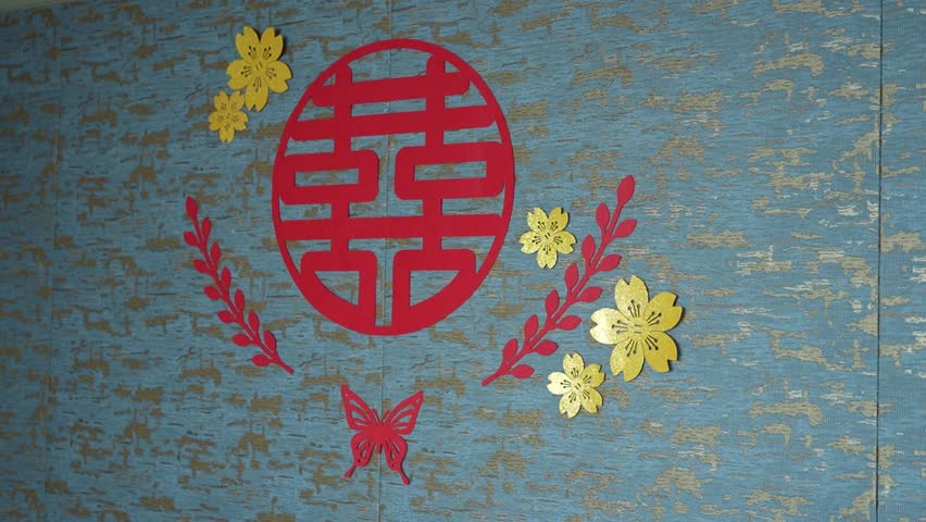 A decorative wall setup featuring a Chinese red double happiness symbol surrounded by golden flowers and other red designs, symbolizing good fortune and celebration,