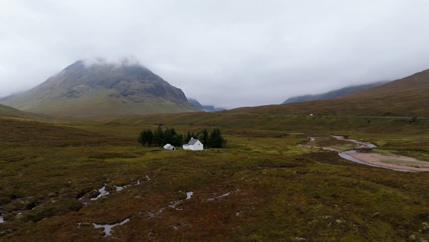 Aerial footage of a cottage and small forest in Glencoe mountain range in the Scottish Highlands