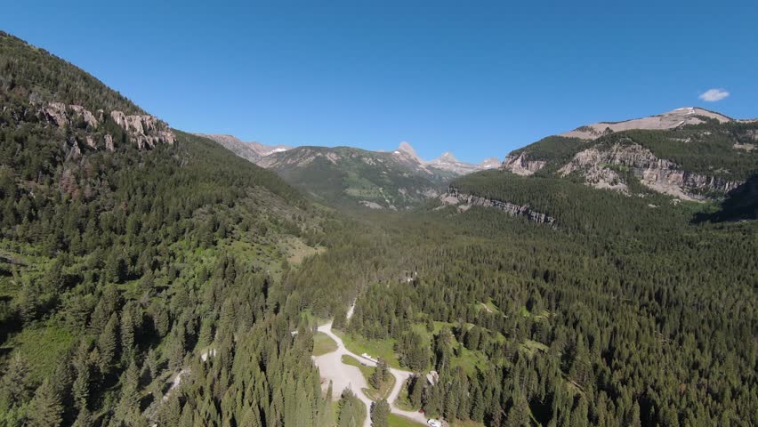 Slow moving forward shot of the Grand Teton National Park, showing the vast forest on the back of the peak. This view of the park shows a beautiful summer weather and vegetation, full of colors