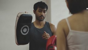 Female athlete wearing boxing gloves practicing boxing by striking boxing pad held by her trainer in gym. Boxing training, fitness, self-defense, combat skills and strength development.  - Powered by Shutterstock - Get 15% off with code: PIKWIZARD15