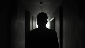 A mysterious silhouette of a man walks down a dimly lit hallway toward a bright light. The contrast of shadows and light creates a cinematic, suspenseful mood, evoking mystery, introspection, and the  - Powered by Shutterstock - Get 15% off with code: PIKWIZARD15