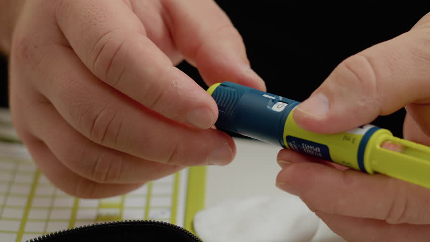 A man prepares an insulin pen to inject medication for managing high blood sugar. He carefully sets the insulin dosage while monitoring his levels with a glucometer.