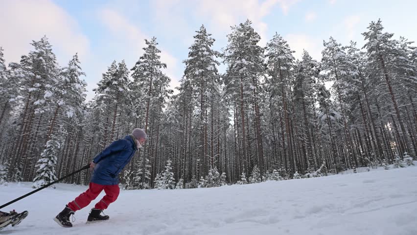 Child pulls an inflatable donut sled with another child on a snowy hill in the forest.