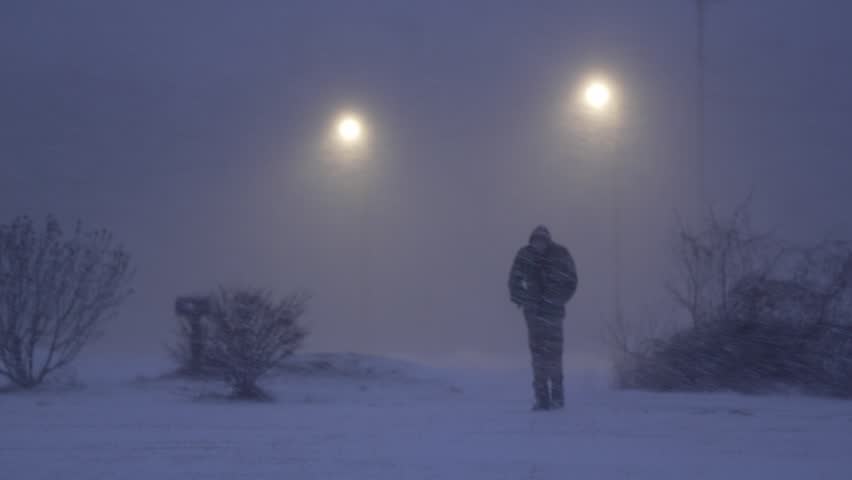 Homeless Man Walks Through Snowy Blizzard with Streetlights in the Background