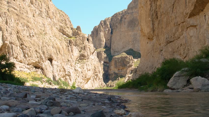 Big Bend National Park - Rio Grande 4K: Slow zoom from the river’s surface shows flowing water, pebbles on the U.S. side, and towering rock mountains on Mexico