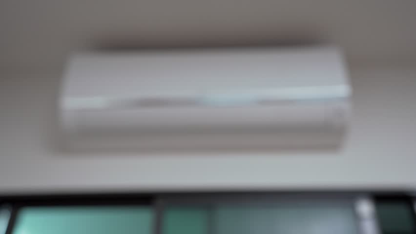 Close up of a hand holding an air conditioner remote pointing it towards to turn it on in a cozy living room at home. Hand using remote controller for adjust Air conditioner