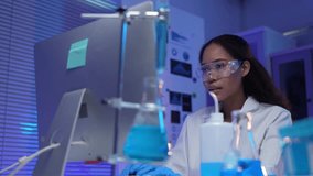 Laboratory technician analyzing data on computer, examining test tubes with blue liquid, wearing lab coat and protective glasses, working late in modern laboratory - Powered by Shutterstock - Get 15% off with code: PIKWIZARD15